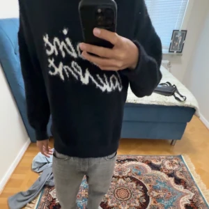 Saint Laurent svart stickad tröja - Svart stickad tröja från Saint Laurent med vit fuzzy logga framtill. Tröjan har en klassisk passform, rund hals och långa ärmar. Mjuk och skön, perfekt för dig som gillar streetstyle med lyxig touch. 