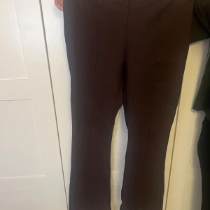 Bruna kostymbyxor från Gina Tricot M - Snygga bruna kostymbyxor från Gina Tricot i storlek M. Byxorna har raka ben med lätt bootcut, pressveck framtill och två fuskfickor bak. Perfekta för en clean och stilren look.