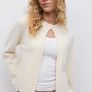 Vit kofta från Gina Tricot - Säljer en stilren vit kofta från Gina Tricot med rund halsringning och en knapp upptill. Koftan är långärmad, har ribbade kanter och är gjord i mjukt stickat material. Perfekt att slänga över en topp eller klänning för en clean look.