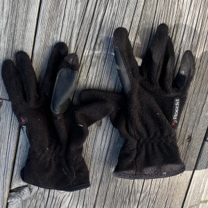 Svarta fleecehandskar från Roeckl - Svarta fleecehandskar från Roeckl med förstärkta greppytor i syntetmaterial på handflatan och fingrarna. Perfekta för kyliga dagar och har en sportig look med Roeckl-logga på ovansidan. Sitter skönt runt handleden och är lätta att ta på.