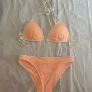 Persikofärgad bikini med vita detaljer från H&M  - Superfin bikini från H&M i en fräsch persikofärg med vita detaljer. Triangeltopp med knyt i nacken och ryggen, samt matchande  bikinitrosor. Perfekt för stranden eller poolen, riktigt somrig vibe! Storlek 34 på underdelen och storlek 38 (passar även 36) på överdelen