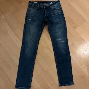 Slim fit jeans från Jack & Jones - Mörkblå slim fit jeans från Jack & Jones, modell Glenn. Jeansen har slitna detaljer på låret och klassisk femficksdesign. Materialet är denim med snygg tvätt och smal passform som sitter tajt längs benen.