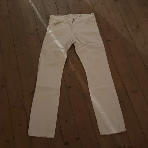 Vita jeansbyxor från ENERGIE, stl 31 - Snygga vita jeansbyxor från ENERGIE i klassisk rak modell. Byxorna har fem fickor, dragkedja och knapp framtill samt diskret röd brodyr vid fickan. Perfekta för dig som vill ha en clean och fräsch look.