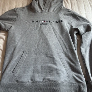 Grå hoodie från Tommy Hilfiger - Säljer min gråa hoodie med broderat tryck från Tommy Hilfiger. Storlek 176 men passar en S/M beroende på hur man vill att den ska sitta. Säljer på grund av att den bara har legat i min garderob ett tag utan användning.