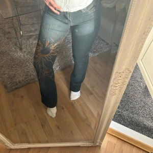 Snygga unika jeans  - Mörkblå jeans med snyggt tryck i orange och svart på ena benet. Klassisk femficksmodell med raka ben och normal passform. Jeansen har medel/låg midja och är tillverkade i slitstarkt denimtyg. Perfekt för dig som vill sticka ut med en cool detalj.