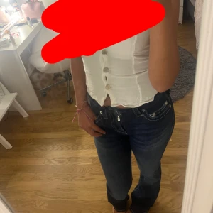 Mörkblå True Religion jeans bootcut - Säljer ett par mörkblå jeans från True Religion med tydliga vita sömmar och klassiska bakfickor med logga. Modellen är lågmidjad/ midrise och har bootcut-ben, vilket ger en snygg siluett. Jeansen är i stretchigt denim och har silverfärgade detaljer vid fickorna. Aldrig använt ute prislappen på, Becca midrise 