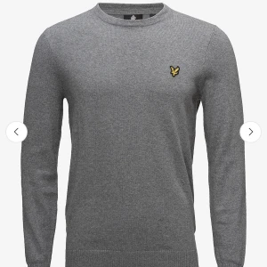 Grå stickad tröja från Lyle & Scott - Snygg grå stickad tröja från Lyle & Scott med rund halsringning och klassisk gul logga på bröstet. Tröjan har lång ärm och ribbade muddar vid ärmslut och nederkant. Perfekt för lager-på-lager under höst och vinter.