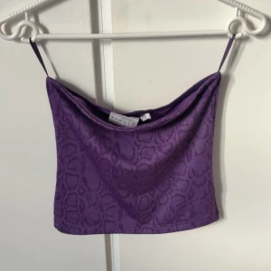 Lila tubtopp med ormmönster  - Säljer en lila tubtopp från Hennes Collection med smala axelband och coolt ormmönster. Toppen har en lätt draperad halsringning och är i ett mjukt, stretchigt material. Perfekt för dig som vill sticka ut med en unik och trendig look. Säljs ej längre och svår att få tag på