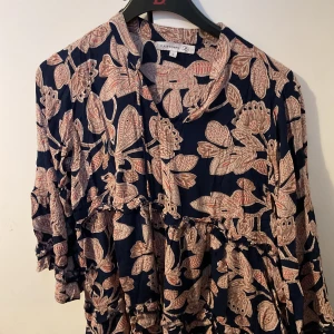 Blommig marinblå klänning från Flash Woman - PRISET KAN DISKUTERA. Säljer en marinblå klänning med blommigt mönster i beige och rosa toner från Flash Woman. Klänningen har volangdetaljer och långa ärmar med lätt puff. Perfekt för dig som gillar boho-vibe och snygga prints. 