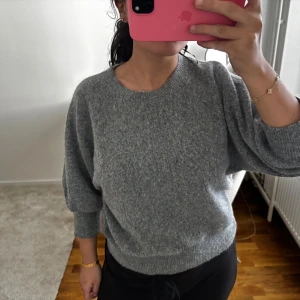 Grå stickad tröja från Lindex - Mysig grå stickad tröja från Lindex med rund halsringning och breda muddar vid ärmslut och nederkant. Tröjan har en loose passform och är perfekt för kyliga dagar. Enkel att matcha med både jeans och kjol.