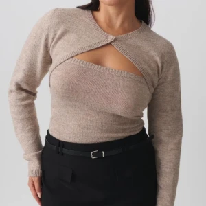 Beige omlott stickad tröja - Trendig beige stickad bolero med två delar. Det är knapp framtill. Långärmad modell med snygg topp med. Perfekt för dig som vill ha en cool och annorlunda look. Mjuk och skön att bära.
