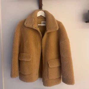 Beige teddyjacka från Zara -  beige teddyjacka från Zara med stor krage och två stora fickor framtill. Jackan har en rak passform och stängs med dragkedja och tryckknappar. 