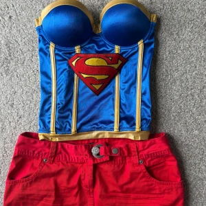 Superwoman blå och gul korsett - Snygg korsett i blått och guld med vadderade kupor och super woman logga framtill. Super söt till halloween, använd 1 gång passar xs/s och skulle säga ca B cupa, kjolen ingår också ”jeans” aktigt material