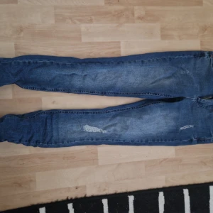 Blå skinny jeans med slitningar - Säljer ett par blå skinny jeans med snygga slitningar på framsidan. Jeansen har klassisk femficksdesign och dragkedja. Perfekta för dig som gillar en tight passform och en trendig, avslappnad look. Storlek s längd 32