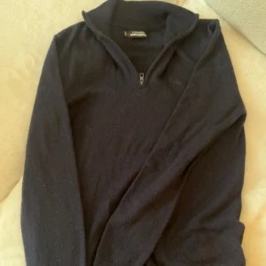 L Lindberg halvzip - Mörkblå stickad tröja från J.Lindeberg med halv dragkedja vid kragen. Klassisk och stilren modell med lång ärm och ribbad krage. Perfekt för lager-på-lager och passar till många olika outfits. S men passar S/xs