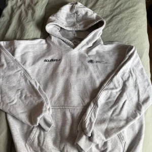 Grå hoodie från Scuffers med tryck - Säljer en ljusgrå hoodie från Scuffers med svart tryck framtill och stort 'withlove'-tryck på ryggen. Klassisk känguruficka, ribbade muddar och huva. Perfekt för chill dagar och streetstyle. Materialet är mjuk bomullsmix som känns skön mot huden.