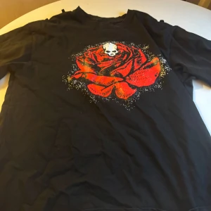 Number nine - Cool svart number nine t-shirt med en stor röd ros och en vit dödskalle tryckt på bröstet. T-shirten har korta ärmar och en klassisk passform. Perfekt för dig som gillar edgy och unika tryck. Materialet känns som bomull och är mjukt mot huden.