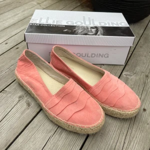 Rosa espadrillos från Ellie Goulding - Snygga espadrillos i ljusrosa tyg från Ellie Goulding Star Collection. Skorna har vågiga sömdetaljer på ovandelen och en klassisk flätad sula i naturmaterial. 
