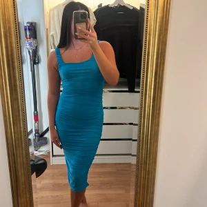 Turkos tight midiklänning - Säljer en turkos tight klänning med rynkade detaljer och breda axelband. Klänningen har en kroppsnära passform och är ärmlös med fyrkantig ringning. Perfekt för dig som vill sticka ut med en färgstark look.