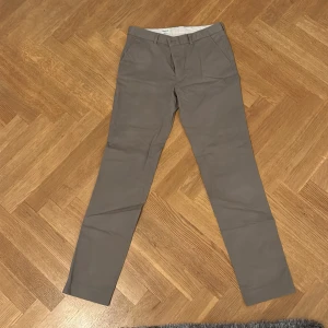 Grå kostymbyxor med rak passform - Snygga grå kostymbyxor med klassisk rak passform och diskreta fickor fram och bak. Perfekta för en clean och stilren look. Byxorna har bälteshällor och stängs med dragkedja och knapp. Passar dig som gillar enkel och tidlös stil.