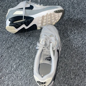 Nike Air Max sneakers i grått - Nike Air Max sneakers i ljusgrå och vit färg med svarta detaljer. Skorna har en chunky sula med synlig Air Max-dämpning, mesh och syntetmaterial på ovandelen samt klassisk snörning. Snyggt sportig look med rund tå och platt sula.