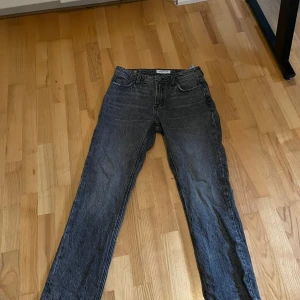 Grå jeans från Smog/Denim 29/32 - Säljer ett par grå jeans från Smog/Denim i storlek 29/32. Jeansen har klassisk femficksdesign, raka ben och normal passform. Materialet är denim och färgen är tvättad grå med en lite sliten look. Perfekta för en avslappnad stil.