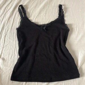 Svart spets linnetopp  - Svart spets linnetopp från H&M Divided med smala axelband och spetskant längs urringningen. Söt liten rosett framtill. Perfekt för lager-på-lager eller som den är. Mjuk och stretchig känsla. 🤗🤗❤️ kontakta för frågor