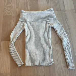 Offshoulder ribbad tröja från Lindex - Säljer en ribbstickad offshoulder-tröja från Lindex i beige. Tröjan har lång ärm och bred, vikt krage som sitter snyggt över axlarna. Tröjan är aldrig använd 