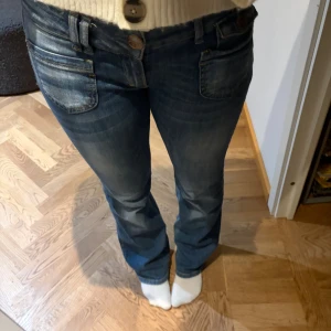 Blå bootcut jeans med låg midja - Snygga blå jeans med bootcut-modell och låg midja. Jeansen har klassiska fickor fram och bak, samt slitningar och tvättade detaljer för en cool look. Perfekta för dig som gillar en avslappnad men trendig stil.