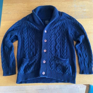 Mörkblå kabelstickad kofta - Mörkblå kabelstickad kofta från SHIPS JET BLUE i storlek medium. Koftan har grovstickat mönster, stora ribbade muddar, två fickor fram och stängs med knappar. Perfekt för lager-på-lager och chill höst- eller vinterstil.