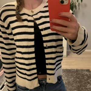 Randig kofta från Gina Tricot - Säljer en stickad kofta från Gina Tricot i svart och vitt med horisontella ränder. Koftan har rund hals, knapp framtill och två små fickor. Från början var det knappar hela vägen ner men jag tog bort de då jag tyckte det var snyggare med bara en! Har en fläck längst ner men den syns knapp och jag tror den går bort i tvätten!