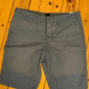Blå bomullsshorts från Blueprint - Snygga blå shorts från Blueprint i klassisk modell med raka ben och bälteshällor. Shortsen har två sidofickor, två bakfickor med knapp och är tillverkade i mjuk bomull. Perfekta för varma dagar och enkel att matcha med t-shirt eller skjorta. Storlek M.