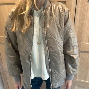 Beige/grön quiltad bomberjacka - Snygg beige/grön bomberjacka med quiltat mönster och dragkedja framtill. Jackan har ribbade muddar vid ärmslut och nederkant, samt en loose passform. Perfekt för dig som gillar en stilren och trendig look. Lånade bilder!