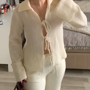 Krämvit stickad kofta med snörning - Superfin krämvit stickad kofta med bred krage och trendig snörning framtill. Helt oanvänd!