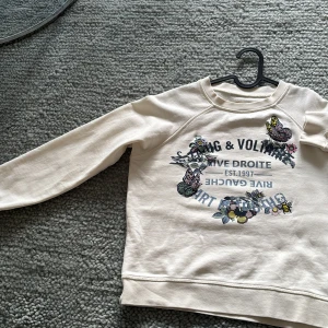 Vit sweatshirt Zadig & Voltaire - Vit sweatshirt från Zadig & Voltaire med broderade blommor, fjäril och bi på framsidan. Tryckt text i blått och svart. Mjuk bomullskänsla, rund hals och långa ärmar. Perfekt för dig som gillar coola detaljer och fräscha färger.