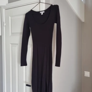 Svart ribbad långärmad klänning H&M XS - Svart långärmad klänning från H&M i ribbat material. Klänningen har en rund, djup ringning och är figurnära med lång siluett. Perfekt för dig som gillar en enkel men stilren look. Materialet är stretchigt och bekvämt.