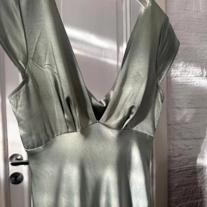 Ljusgrön långklänning från Hello Molly - Säljer en ljusgrön långklänning från Hello Molly i glansigt satin material. Klänningen har v-ringnin och, öppen rygg. Den har använts en gång, har några repor man absolut inte tänker på