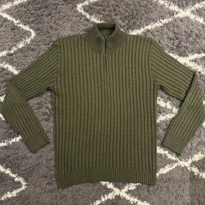 Olivgrön half zip tröja - Säljer en olivgrön ribbstickad tröja med half zip och hög krage. Tröjan har lång ärm och är i ett mjukt, stickat material som ger en clean och stilren look. Jag är 180cm,67kg och den passar mig perfekt.