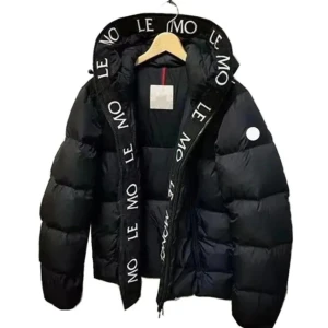 Svart Moncler pufferjacka med huva - Svart pufferjacka från Moncler med stor huva och tydlig logotyptext längs insidan av huvan. Jackan har en quiltad design, dragkedja framtill och en rund vit logodetalj på ärmen. Perfekt för kalla dagar och riktigt snygg streetstil.