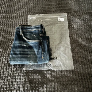 Blå dsquard jeans  - Säljer ett par blå jeans från Dsquared2 med slitna detaljer och snygg tvätt. Jeansen har klassisk femficksdesign, orange sömmar och Dsquared2-lapp bak i midjan. Modellen är smal och har en modern, tight passform.