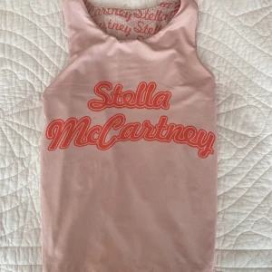 Rosa linnetopp Stella McCartney - Säljer en rosa ärmlös linnetopp från Stella McCartney med coolt tryck framtill (och funkar även att vända ut och in) med all-over logomönster på insidan. Toppen är i sportig mesh och har korallröda detaljer. Perfekt för dig som gillar statement-plagg och sportig stil.