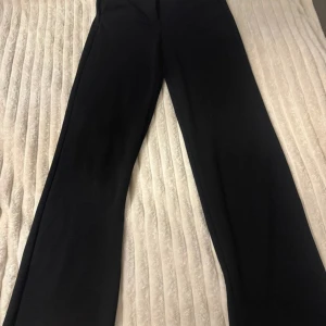 Svarta kostymbyxor från Vero Moda - Stilrena svarta kostymbyxor från Vero Moda med raka ben och klassisk passform. Byxorna har hällor för bälte och stängs med dold dragkedja fram. Perfekta för en clean och snygg look.