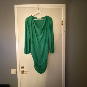 Grön draperad klänning Sisters Point - Snygg grön kortklänning från Sisters Point med draperad framsida och långa ärmar. Klänningen har en lösare passform upptill, markerad midja och cool rynkdetalj nedtill. Perfekt för dig som vill sticka ut med en färgstark look.💚Frakt ingår inte 