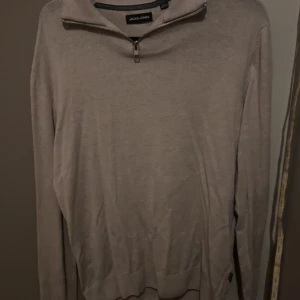 Beige half zip-tröja Jack & Jones - Snygg beige långärmad tröja från Jack & Jones med half zip-dragkedja i halsen. Tröjan har en klassisk passform och är tillverkad i mjuk bomull, perfekt för lager-på-lager under höst och vår.