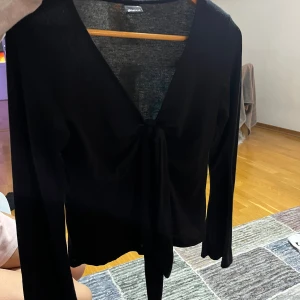 Svart långärmad knytblus Gina Tricot - Svart långärmad blus från Gina Tricot med djup v-ringning och knyt framtill. Tunn och lätt i materialet, perfekt för lager-på-lager. Snygg och enkel att styla till olika looks.