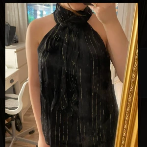 Svart halterneck topp med knyt - Säljer en svart halterneck topp med tunna guldiga ränder och knyt runt halsen. Aldrig använd!