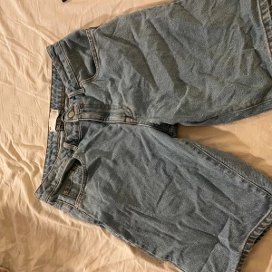 Blå denimshorts med baggy passform - Säljer ett par klassiska blå denimshorts i rak modell. Shortsen har normalhög midja, knapp och dragkedja framtill samt fickor både fram och bak. Perfekta för varma dagar och enkel att matcha med allt. Storlek:32
