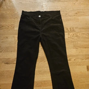 Svarta manchesterbyxor bootcut - Svarta manchesterbyxor med klassisk femficksdesign och bootcut-ben. Byxorna har normal midja och är tillverkade i mjuk manchester som ger en snygg retrovibe. Perfekta för dig som gillar en avslappnad men ändå stilren look. Mått: midja 45 cm, innersöm 76 cm, benöppning 23 cm.