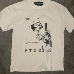 Vit t-shirt Enfants Riches Déprimés M - Vit t-shirt från Enfants Riches Déprimés i bomull med svart grafiskt tryck på framsidan där det står 'TRUE LOVE STORIES' och en sjuksköterska med spruta. Klassisk passform och rund hals. Perfekt statement-plagg för dig som gillar edgy och unik stil.