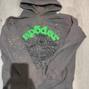 Sp5der hoodie S - Grå hoodie från Sp5der med stor grön logga och svart spindelnätsmönster på bröstet. Hoodien har huva, ribbade muddar och vita samt gröna stjärndetaljer på ärmen. Tillverkad i bomull och har en avslappnad passform.